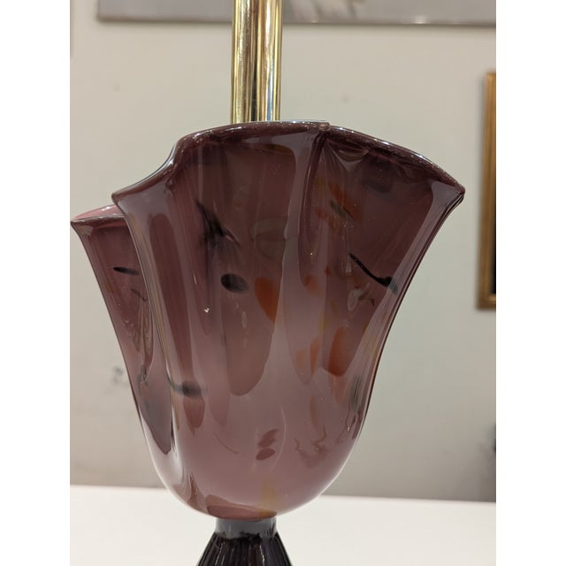 A contemporary lamp featuring a hand-blown amethyst bloom, black conical base, and polished brass pedestal. The white drum...