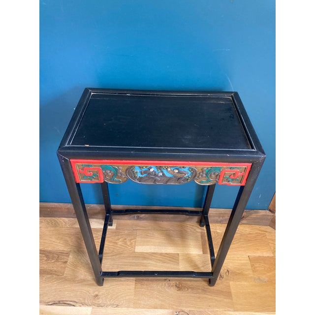 This unique vintage accent table showcases an ornate hand-carved and painted front panel depicting a traditional Asian...