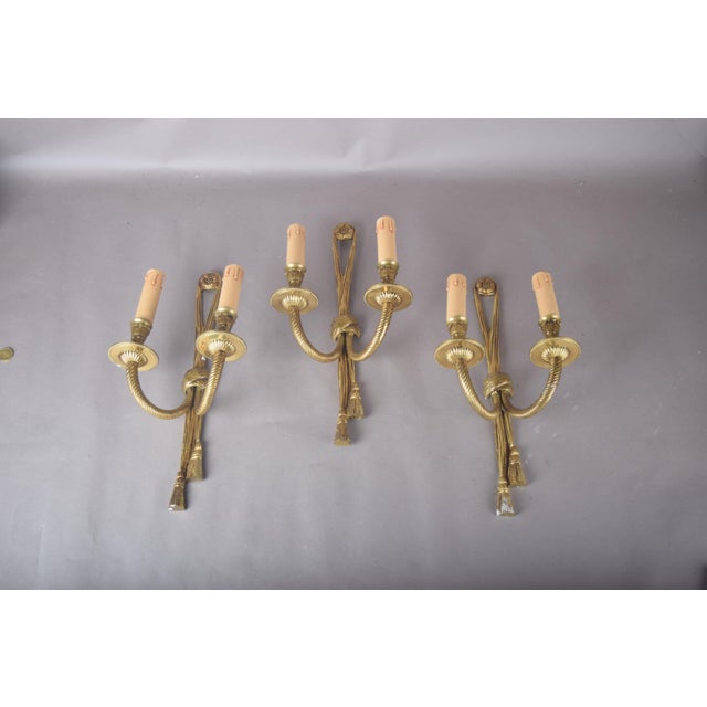 Set of three brass wall sconces with a rope-and-tassel motif. Each has two curved arms springing from a central knot,...