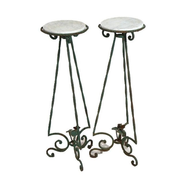 An antique pair of plant stands in the manner of Oscar Bach offer circular marble displays over wrought iron base having...