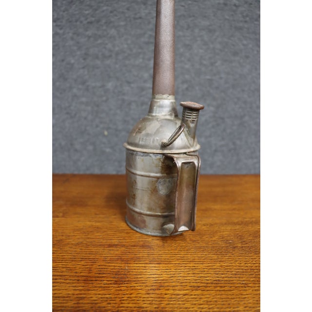 Antique metal oil can featuring a cylindrical body, fitted handle, domed shoulder, and exceptionally long, narrow curved...