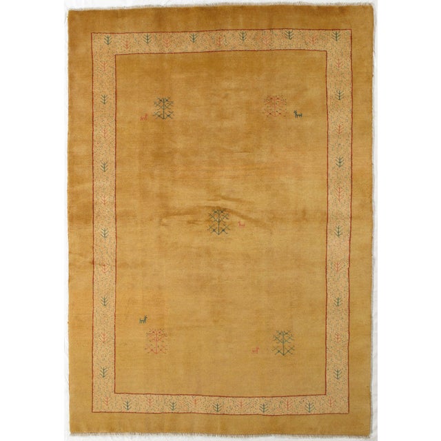 Vintage hand-knotted Persian Gabbeh rug featuring a warm golden field with a simple border and scattered tree and animal...