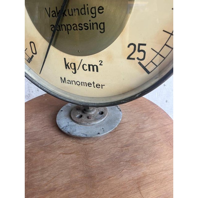 An authentic mid-century industrial pressure gauge featuring a large circular dial housed in a heavy steel casing....