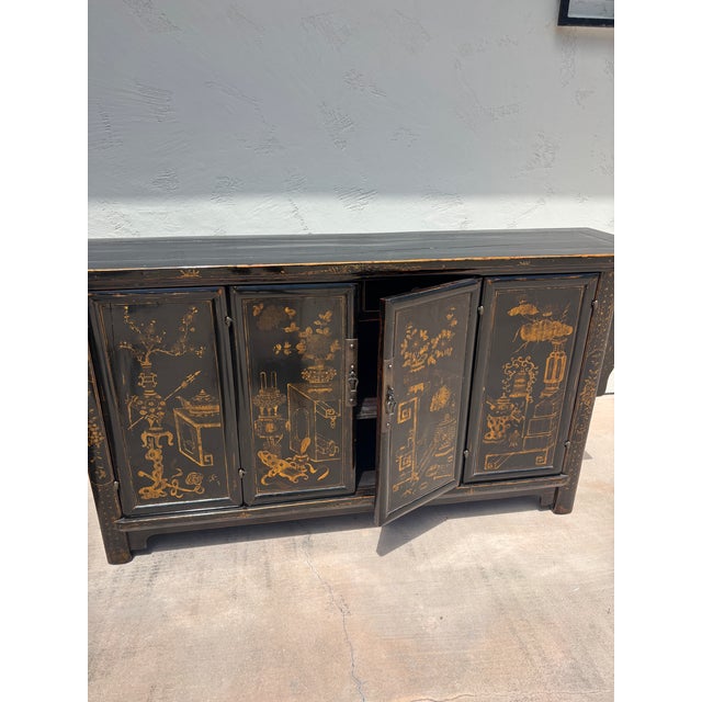 A striking vintage Chinese black lacquer sideboard showcasing beautifully hand-painted gilt decoration inspired by the...