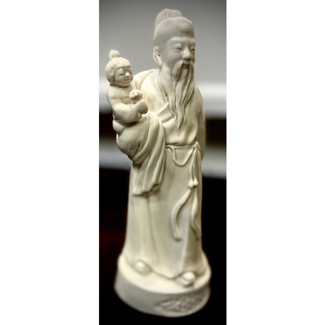 figurine depicts a wise man or immortal holding a child. Dehua porcelain figures often represent revered figures from...