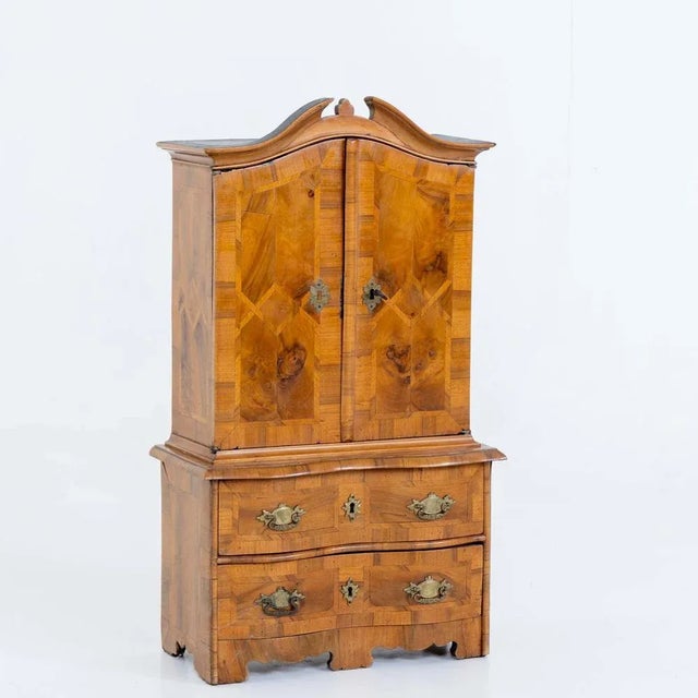 Two-door miniature top furniture with two-drawer dresser base and broken pediment top. The body is veneered in walnut and...