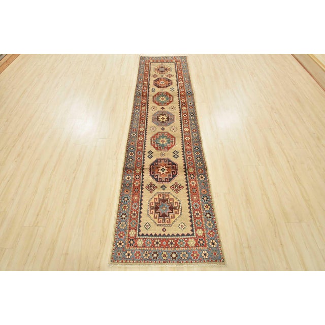 A tribal Caucasian Kazak runner hand-knotted with an all-wool pile on a cotton foundation. This oriental rug features a...