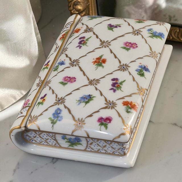 This vintage heirloom trinket box is a beautifully hand-painted porcelain piece in the shape of a book, adorned with a...