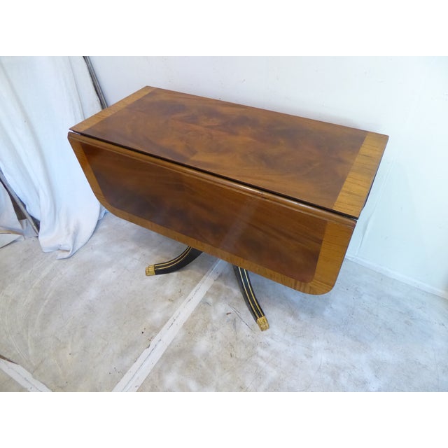 This Regency style drop leaf table has gilded detailing on the legs which are black, and drawers and has brass feet. The...