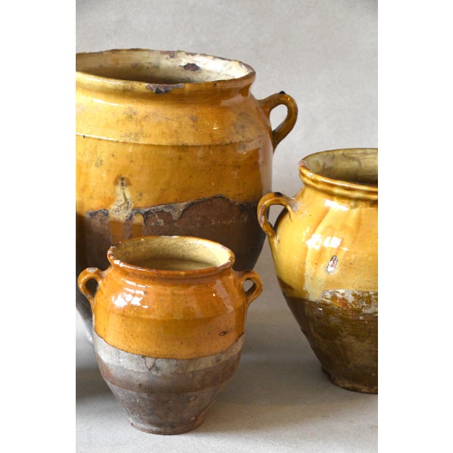 An antique French confit jar in glazed earthenware, dipped halfway in a warm ochre glaze over a bare terracotta base, with...