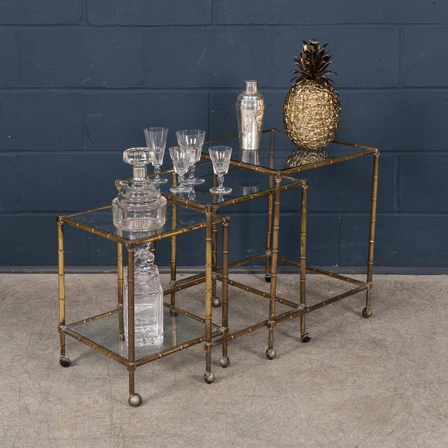 A stylish set of maison jansen faux bamboo nesting tables, featuring brass frames with clear glass tops and lower tiers....