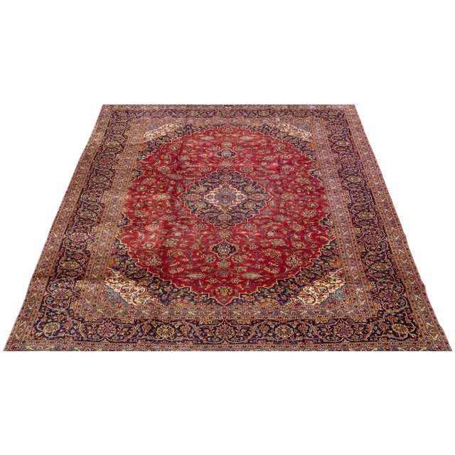 Beautiful vintage Persian Kashan hand-knotted wool rug with a red color field. This piece has a navy blue frame and...