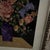 A vibrant fabric collage depicting a bouquet of roses, lilacs, and wildflowers in a purple vase, set against a diamond-...