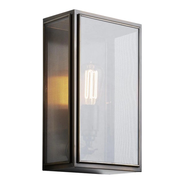 Wall light in brass with outside fitted clear glass and spring closure. Gauze: (removable) woven metal gauze at the inside...