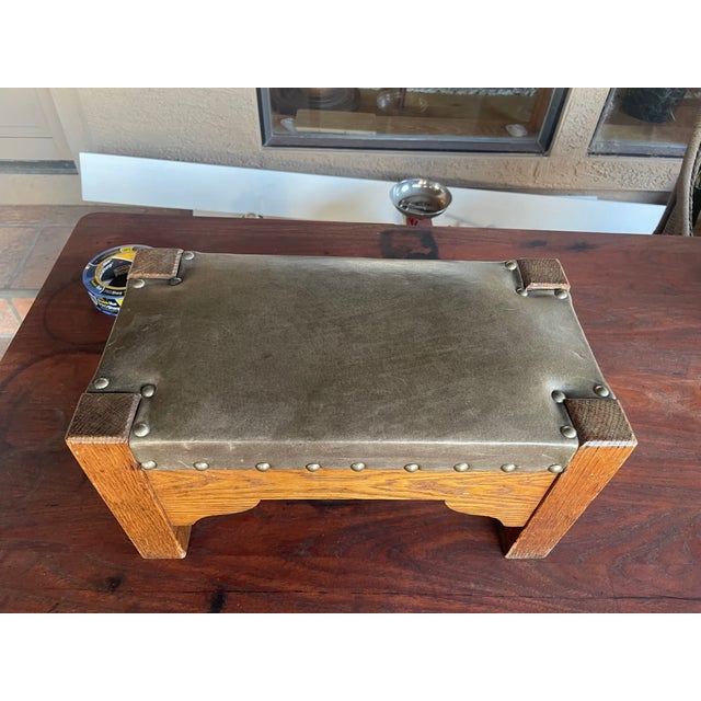 Here is an antique Arts and Crafts/Mission-style oak footstool with green leather secured by decorative metal tacks,...
