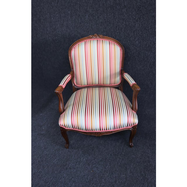 French Style Walnut Carved Open Armchair, crest with floral decoration, striped upholstery, legs and skirt with floral...