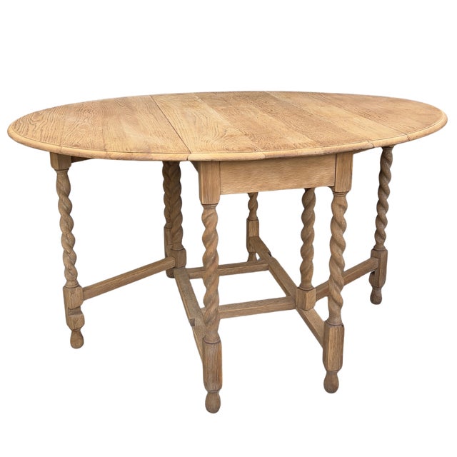 A gorgeous bleached oak folding gateleg table from England, circa 1920. Filled with old-world charm, the carved details...