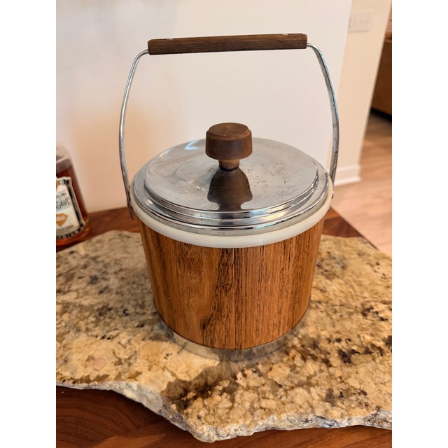 Vintage Kromex insulated ice bucket featuring a faux walnut woodgrain exterior, chrome-plated lid and trim, and original...