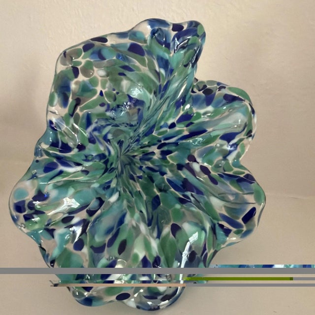This hand-blown Murano style glass flower figurine features a vibrant green and blue color with a confetti style design....