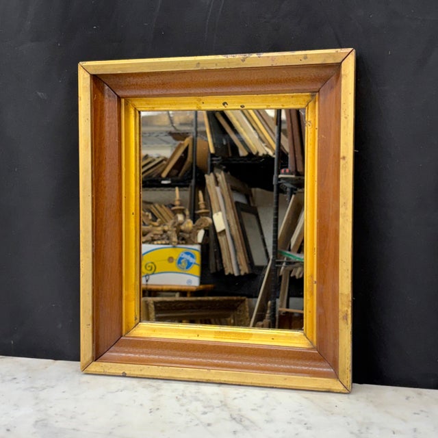 Elegant antique walnut wall mirror with warm wood grain accented by contrasting lemon gilt moldings and an aged gold...