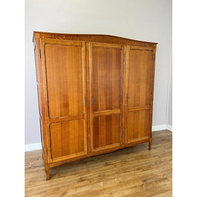 A handsome Vintage French Louis wardrobe crafted in oak, featuring a broad three-door form, warm natural finish and...