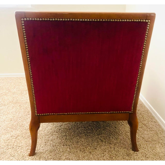 A stunning antique accent chair features a rich deep red tufted upholstery with button detailing, framed by elegant wooden...