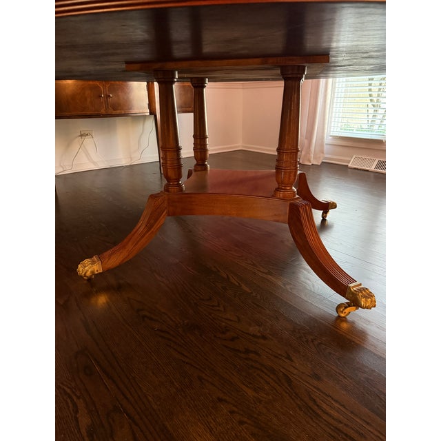 A vintage 72" round mahogany banded dining table by Councill Furniture. It features inlaid trim, brass feet and the...