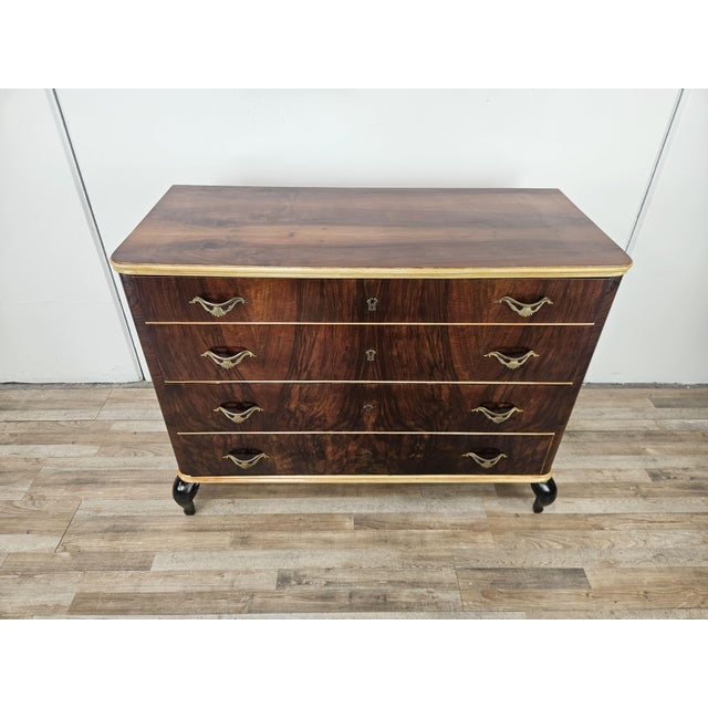Italian 1950s chest of drawers clad in mahogany burl with maple trim and details, enhanced by lacquered legs and brass...