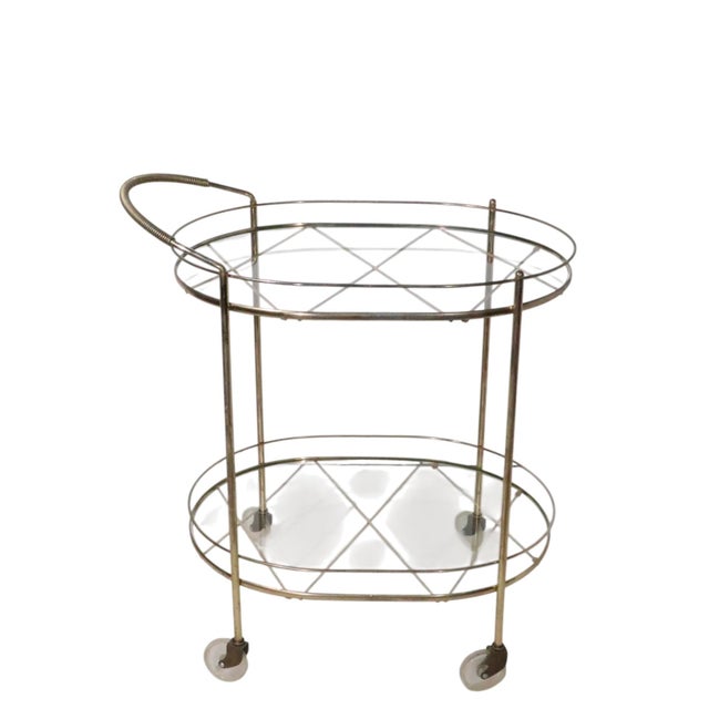 Chic Mid Century Hollywood Regency style rolling bar cart. The cart features two oval glass shelf surfaces, supported...
