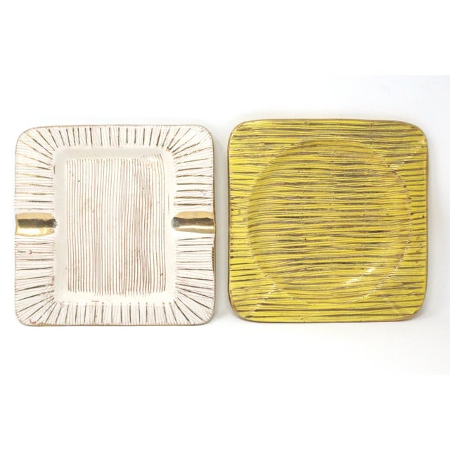 A vintage set of two similar square mid-century ashtrays, one white and one yellow, both with gold linear designs. Good...