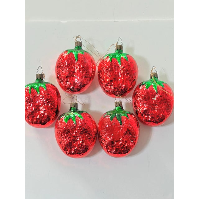 A playful set of large strawberry-shaped mercury glass Christmas ornaments featuring vibrant red bodies with bright green...