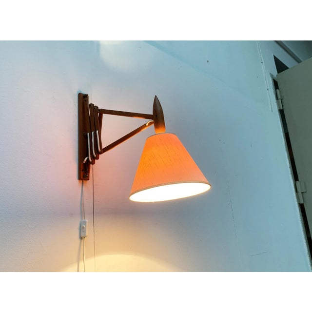 Wall lamp with flexible scissor arm from the Danish lighting manufacturer Le Klint. The lamp is composed of teak solid...