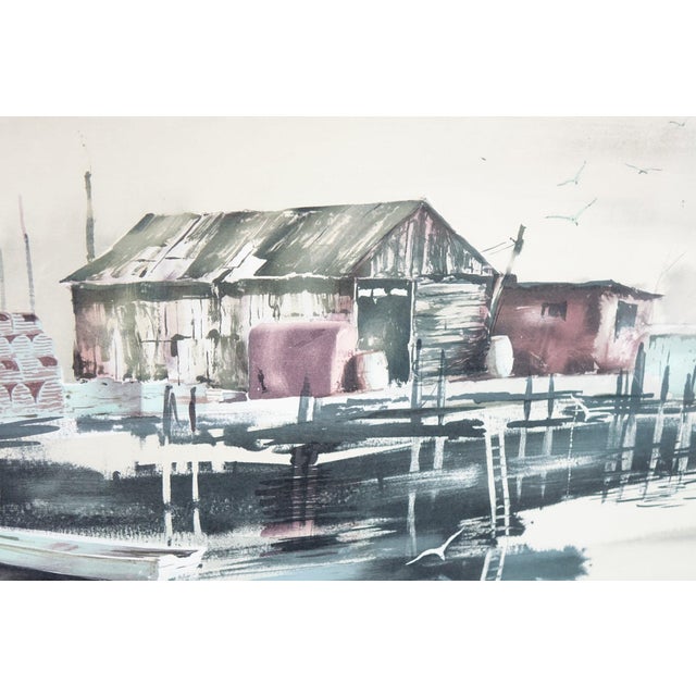 This signed lithograph features a white background that accentuates a detailed depiction of a dock with boats, creating a...