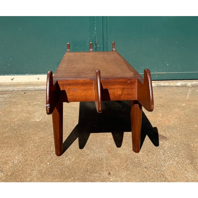Long, low and narrow wood bench with sculptural tapered ends, and legs. Possibly walnut wood with a masonite top. The...
