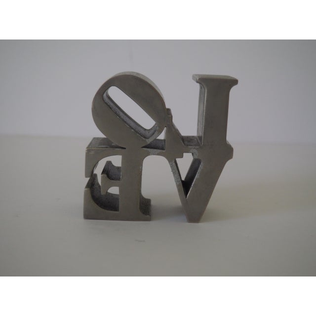 An unmarked, vintage brushed chrome paperweight after the Robert Indiana "LOVE" sculpture. Dimensions: 3"W x 1.5"D x 3"H...