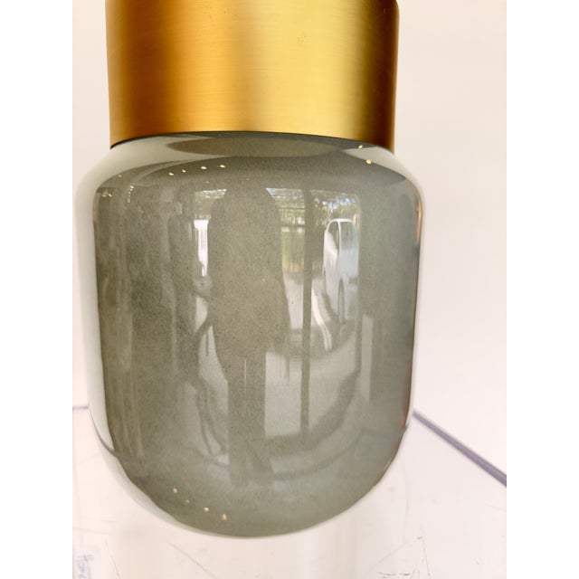 Contemporary decorative accent featuring an opalescent green glass vessel paired with a warm brass rim for a refined...