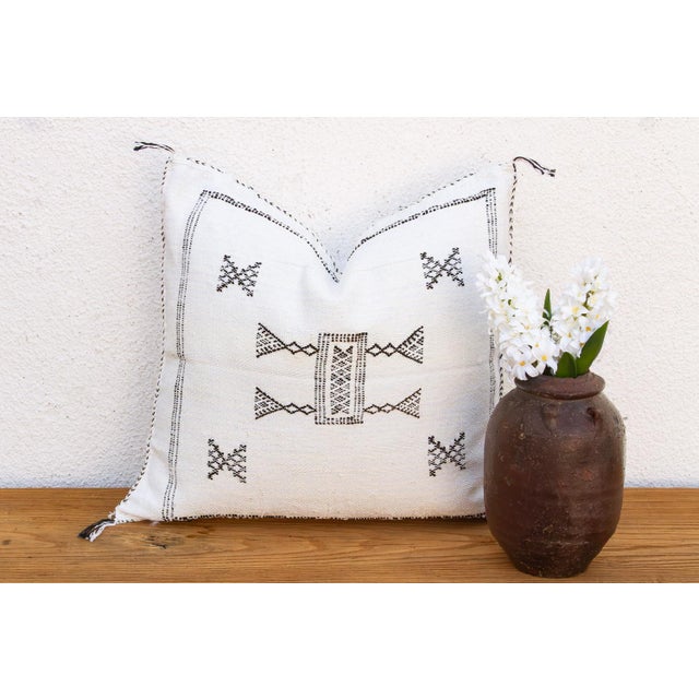 A bowtie-shaped medallion sits at the center of this handcrafted Moroccan cactus silk pillow, framed by a stitched border...