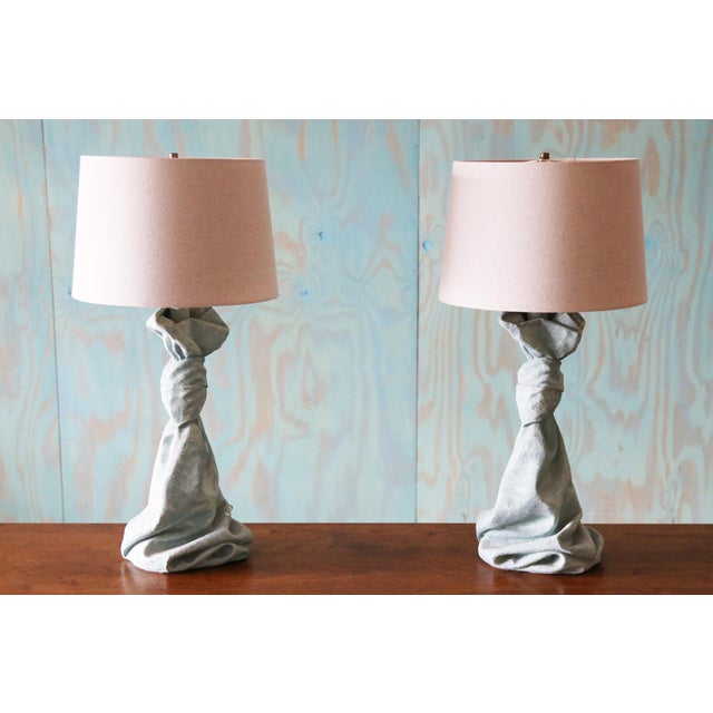 A pair of heavy plaster table lamps featuring a Trompe l'Oeil design that mimics the elegance of knotted, draped fabric....
