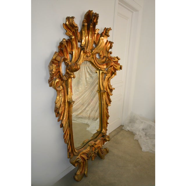 A dramatic statement piece, this monumental giltwood mirror captures the elegance of Rococo revival design, likely Italian...