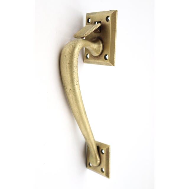 Vintage brass thumb latch door pull with a curved shaped handle and square plates. The original mounting screws are not...