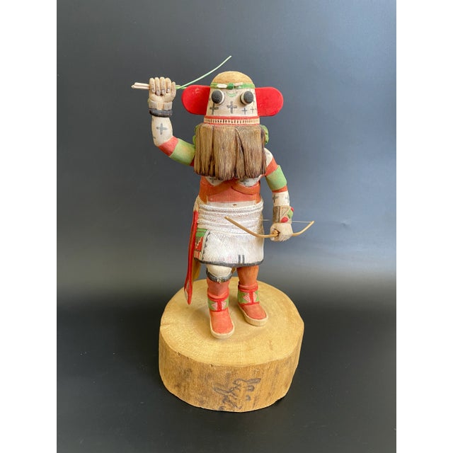 An early Broadface Kachina crafted by the renowned Hopi carver Kevin Pochoema. The Kachina doll carries a bow in one hand...