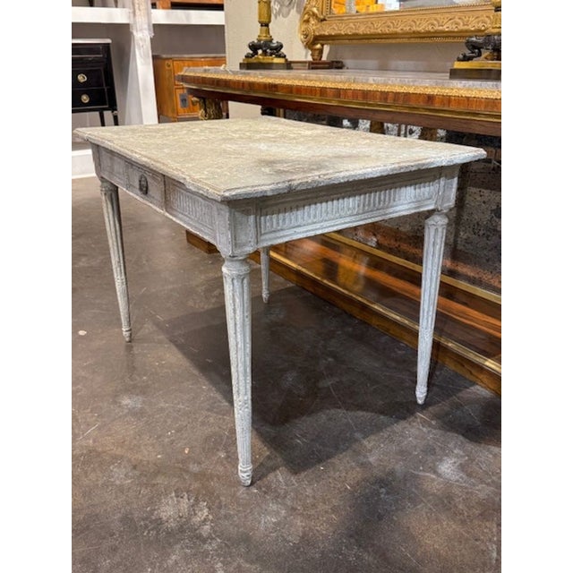 The 19th Century Carved and Painted Louis XVI Writing Table is a lovely piece of antique furniture that showcases the...