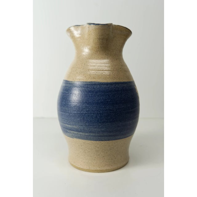 A studio pottery hand crafted pitcher in beige with a blue band and stenciled leaf detail. Signed on the bottom "Wind...