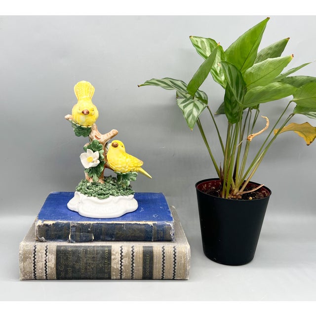 A cheerful Italian ceramic figurine featuring two bright yellow birds perched on a branching tree adorned with green...