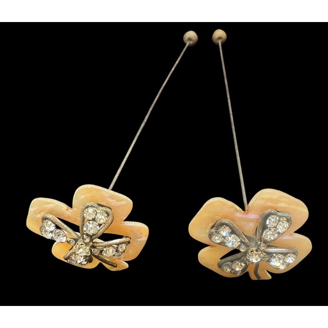 A striking pair of Edwardian hatpins (c. 1895-1915) featuring hand-carved mother-of-pearl clovers set with early cut-glass...