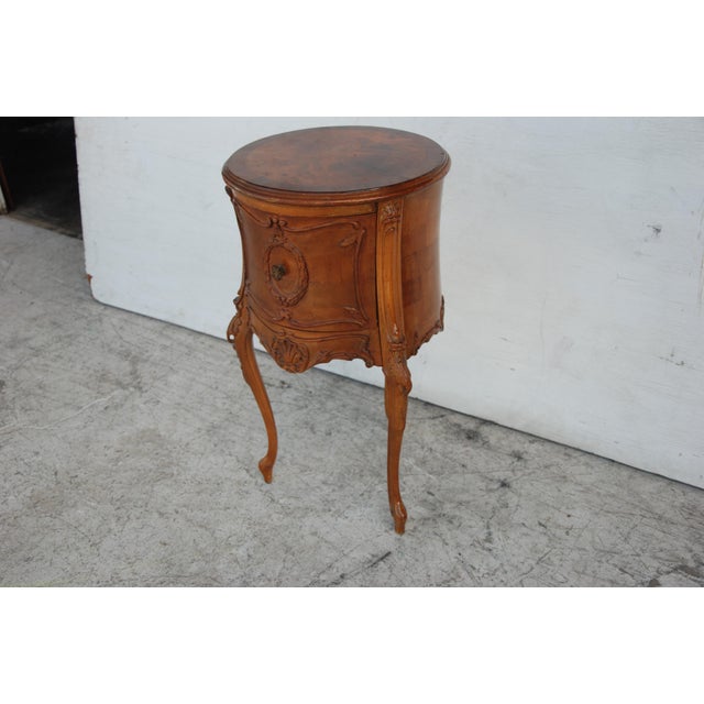 A round nightstand with a burl top, scroll and carved sides with single drawer on cabriole legs.