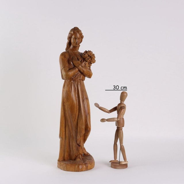 Olive wood sculpture depicting a young woman with a bunch of flowers. This piece is attributed to the mentioned...