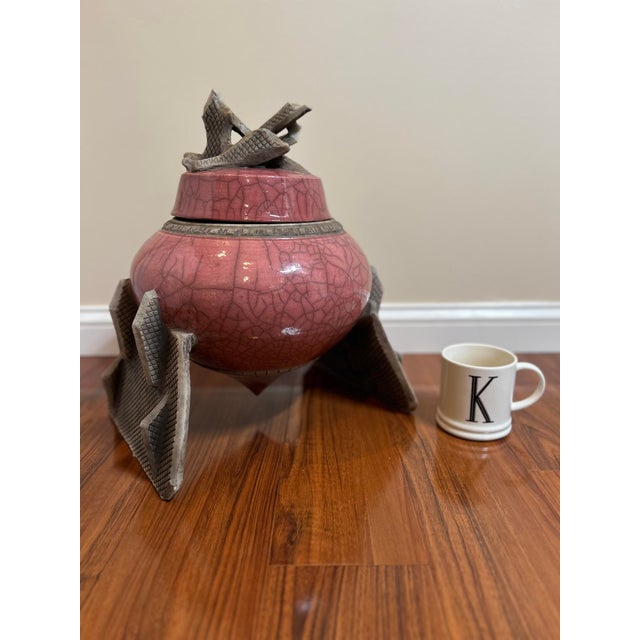 Signed MDC, this vintage raku-fired ceramic vessel pairs a rounded pink crackle-glazed body with angular gray tripod...