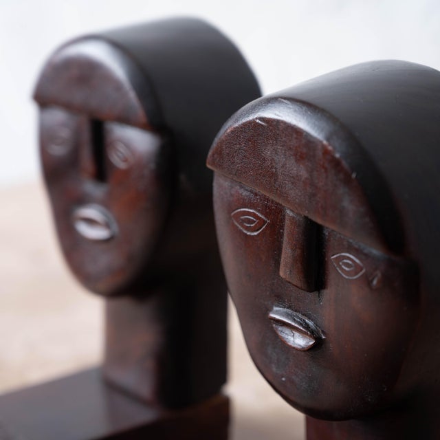 A pair of carved wood bookends from Haiti, circa 1960, each fashioned as a stylized figural head with an elongated crown...