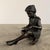 A beautifully cast bronze sculpture of a young girl seated quietly with a book, captured in a moment of calm...